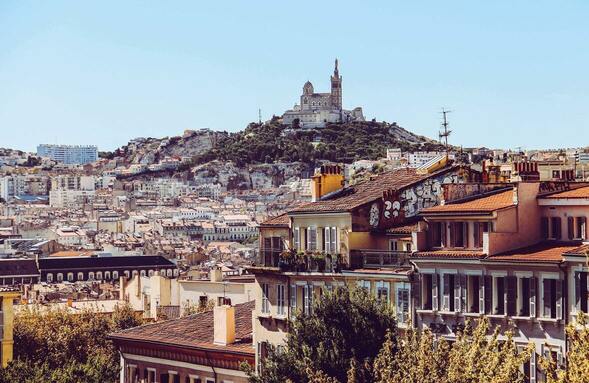 Notre-Dame-de-la-Garde - Paysage avec au premier plan des habitations et au second plan une colline sur laquelle est située la Basilique