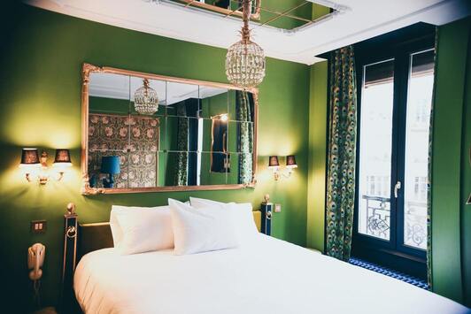 Hôtel Le soleil du matin - Chambre équipée d'un lit de 2 personnes
               (avec tapisserie verte et rideaux verts) et d'un miroir mosaïque, avec fenêtre vue sur la ville